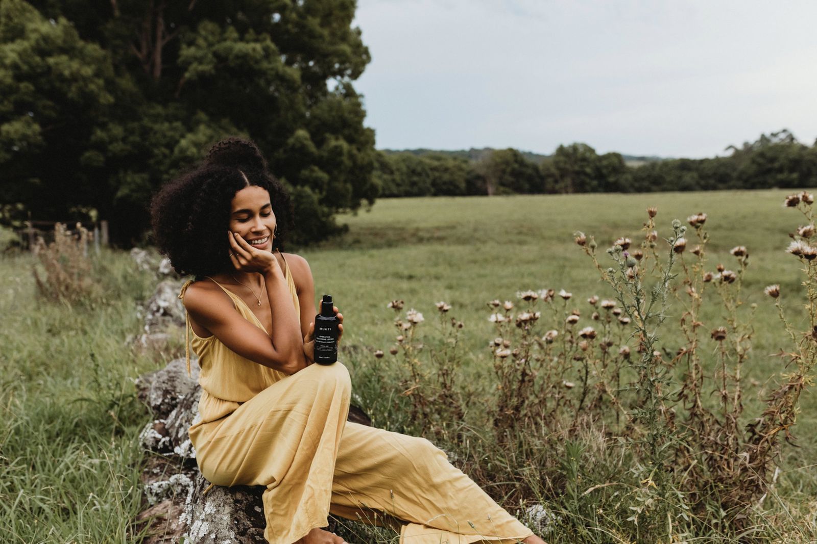 Woman holding Mukti Organics certified organic skincare in a field